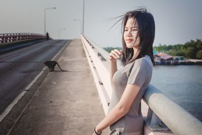 Portrait of young woman sitting on car against sky