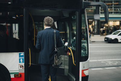 Rear view of male entrepreneur entering bus during business trip in city