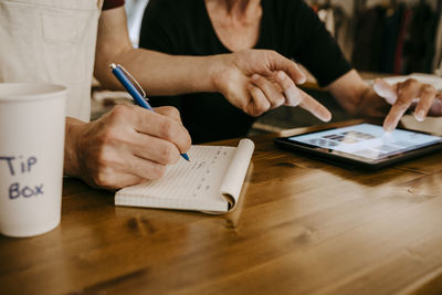 Midsection of owners working while using digital tablet in coffee shop