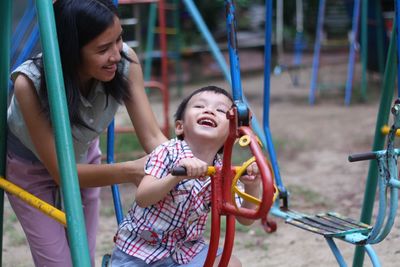 Mother with cheerful son sitting on play equipment at playground