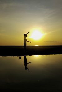 Silhouette man standing by lake against sky during sunset