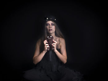 Portrait of young woman standing against black background