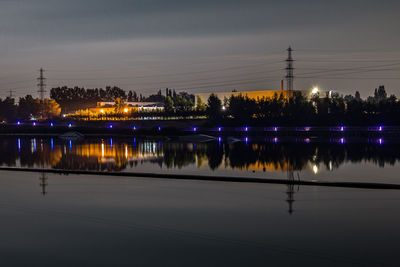 Illuminated city by river against sky at night