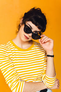 Portrait of young woman wearing sunglasses against orange background