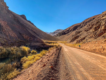 Dirt road amidst mountains against clear sky