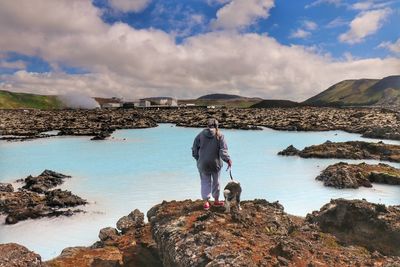 Rear view of girl with dog standing on rocks by lake at blue lagoon