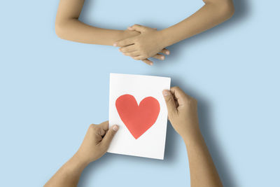 Cropped image of man holding paper with heart shape by hands on table