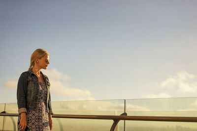 Woman standing by railing against sky