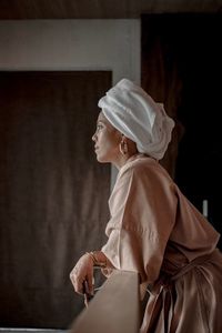 Woman wearing bathrobe and looking away while standing by railing at home