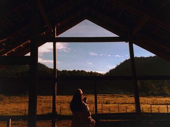 Rear view of woman standing in built structure against landscape during sunset