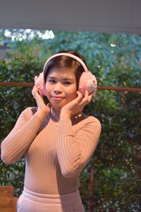 Portrait of young woman wearing ear muff while standing against plants