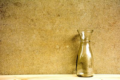 Close-up of glass bottle on table against wall