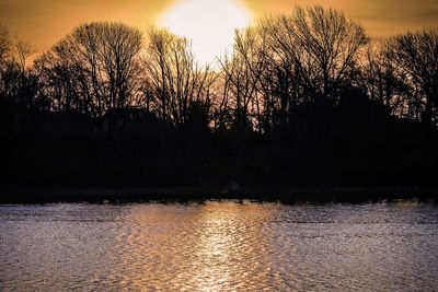Silhouette trees by lake against sky during sunset