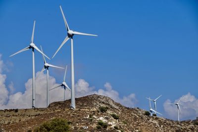 Low angle view of wind turbines against cloudy sky