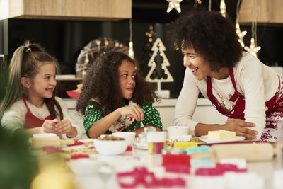 Smiling girls making dough with mother at home