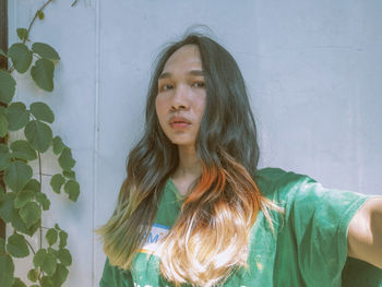 Portrait of young woman standing against wall