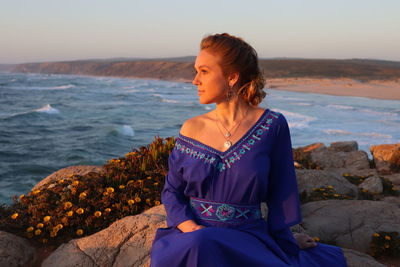 Woman sitting on rock looking at sea against sky