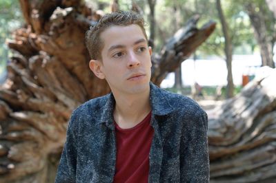 Portrait of young man standing against tree in forest