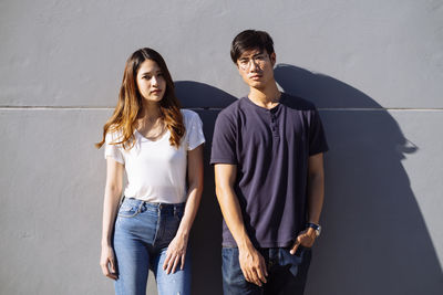 Portrait of young couple standing against wall