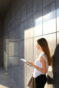 Side view of young woman standing against wall