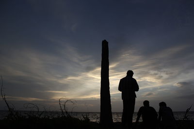 Silhouette people standing on beach against sky during sunset