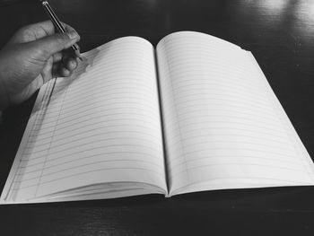 Cropped hand of person holding pencil over book on table