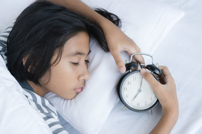 High angle view of girl with alarm clock sleeping on bed