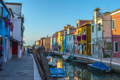 Boats moored in canal amidst buildings against clear sky