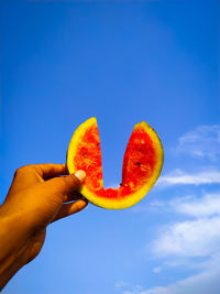 Cropped image of hand holding fruit against blue sky