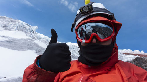 Climber with helmet, headlamp and red jacket taking a selfie on a glacier on a cloudy day, landscape