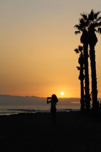 Silhouette woman standing on beach against sky during sunset