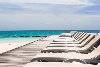 Empty chairs by swimming pool against sky