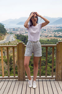 Woman in a white t-shirt and stripe shorts and sunglasses fence a sea view of  mountain in marmaris