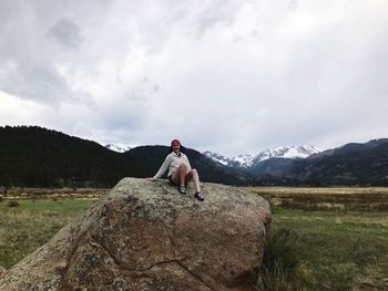 Young woman sitting on rock against cloudy sky