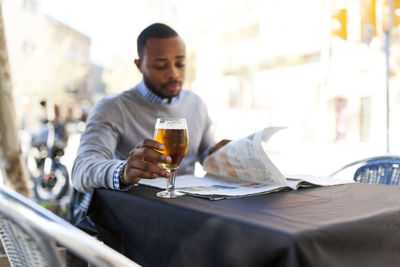 Young man reading newspaper and drinking a beer at street cafe
