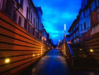 Illuminated street amidst buildings against sky at dusk