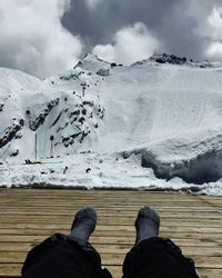 Low section of person on boardwalk against snowcapped mountain