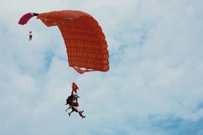 Low angle view of people paragliding against sky