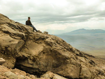 Man standing on rock at mountain against cloudy sky