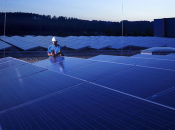 Worker with measuring device checking solar plant in the evening