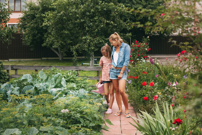 Cute teenage girl with her mother works in the garden, watering flowers and flower beds. 