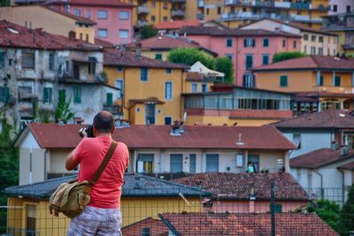 Rear view of mature man photographing houses in city