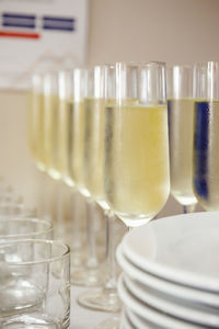 Glasses filled with champagne stand in a row against the background of a wall and white plates