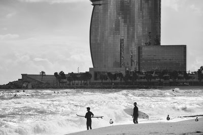 People with surfboards on beach against building