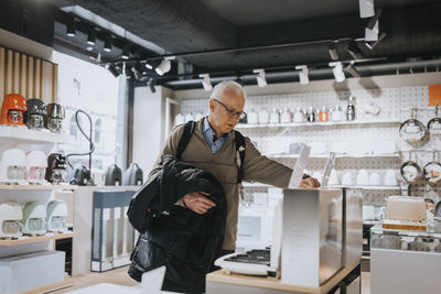 Elderly male customer examining appliance while shopping in appliances store