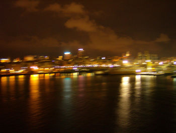 Illuminated city by river against sky at night