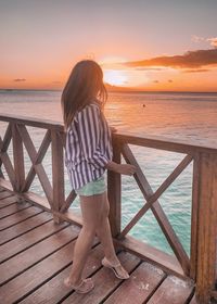 Rear view of woman looking at sea against sky during sunset