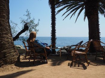 Woman sitting on chair against sea at beach