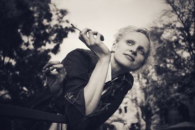 Mid adult woman holding cigarette while leaning on railing 