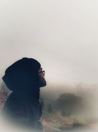 Man looking away sitting against foggy landscape